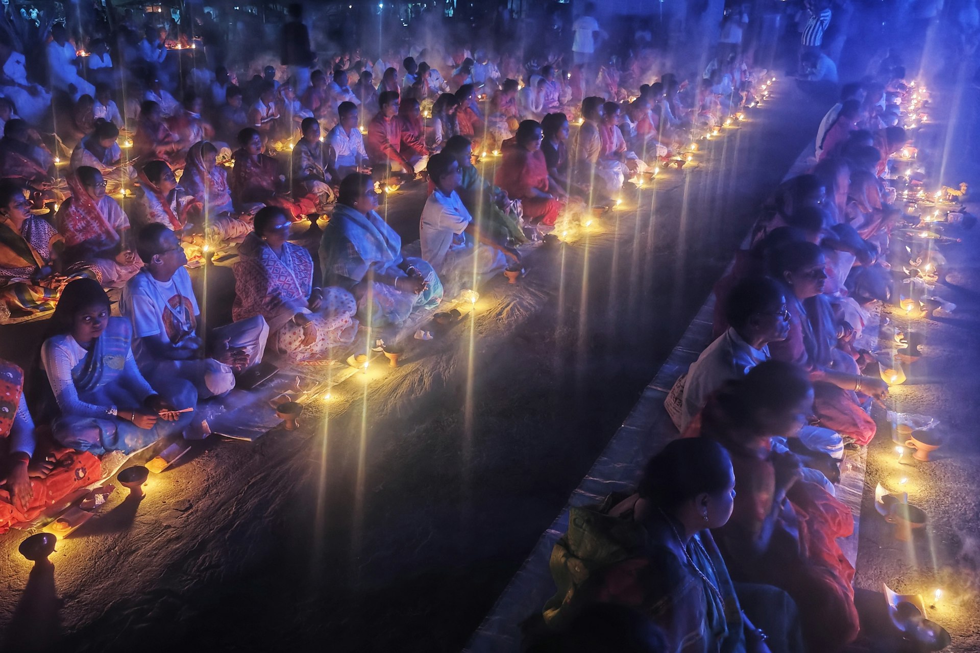 A large group of people sitting in a room with candles